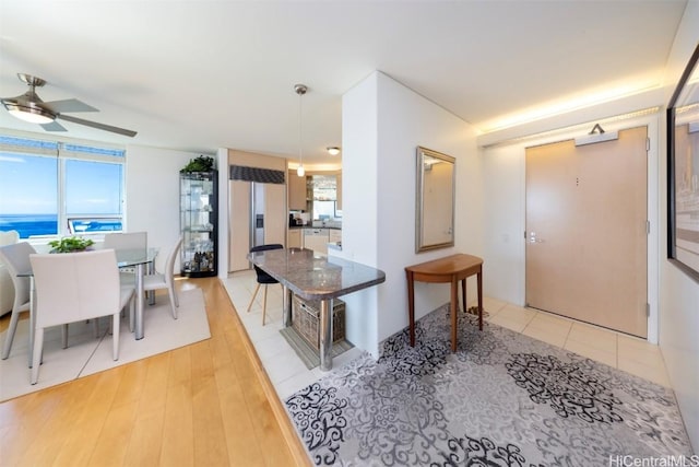 kitchen with light tile patterned floors, ceiling fan, a kitchen breakfast bar, a water view, and decorative light fixtures