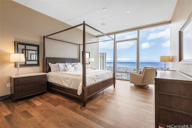 bedroom featuring floor to ceiling windows, a water view, and hardwood / wood-style floors