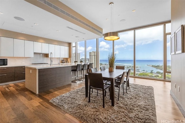 dining space featuring dark wood-type flooring, a wall of windows, and a water view