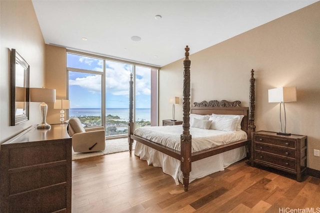 bedroom with wood-type flooring, a water view, access to outside, and a wall of windows