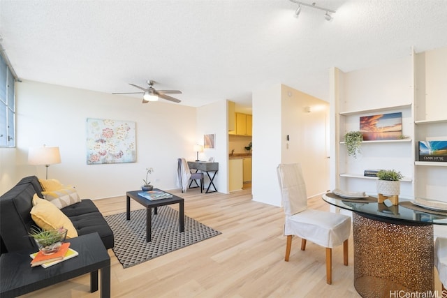 living room featuring ceiling fan, rail lighting, a textured ceiling, and light wood-type flooring