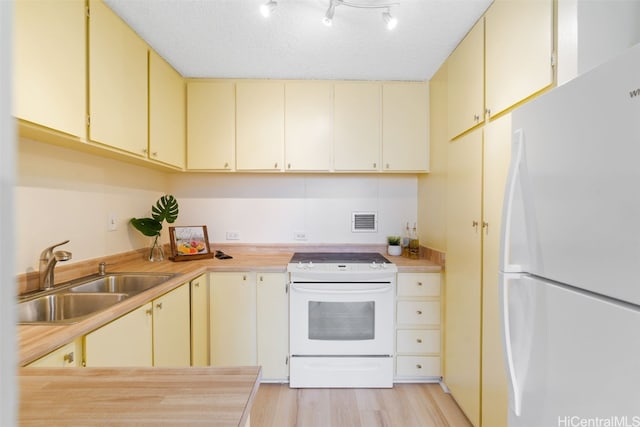 kitchen with sink, white appliances, light hardwood / wood-style flooring, a textured ceiling, and cream cabinetry