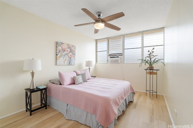 bedroom with cooling unit, ceiling fan, light hardwood / wood-style floors, and a textured ceiling