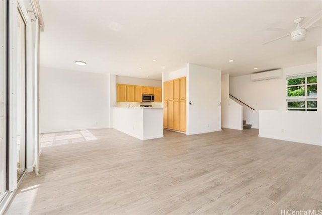 unfurnished living room featuring a wall unit AC, light hardwood / wood-style floors, and ceiling fan