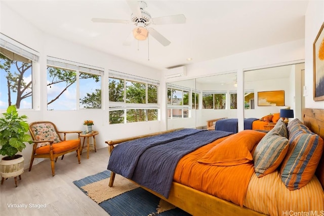 bedroom featuring multiple windows, ceiling fan, light hardwood / wood-style flooring, and a wall mounted AC