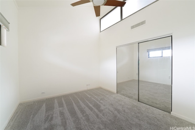 unfurnished bedroom with carpet floors, a closet, visible vents, and a towering ceiling