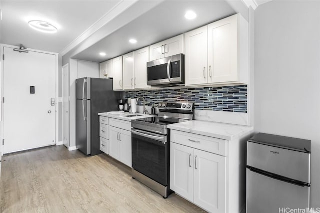 kitchen with appliances with stainless steel finishes, white cabinetry, tasteful backsplash, light stone countertops, and light hardwood / wood-style floors