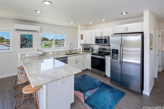 kitchen with appliances with stainless steel finishes, an AC wall unit, a breakfast bar, sink, and light stone countertops