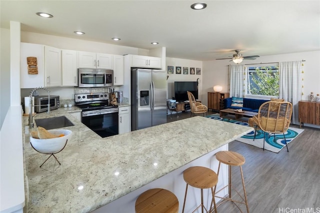 kitchen with light stone counters, appliances with stainless steel finishes, kitchen peninsula, hardwood / wood-style floors, and white cabinets