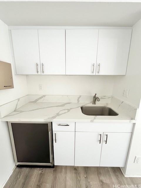 kitchen featuring hardwood / wood-style flooring, white cabinetry, sink, and light stone counters