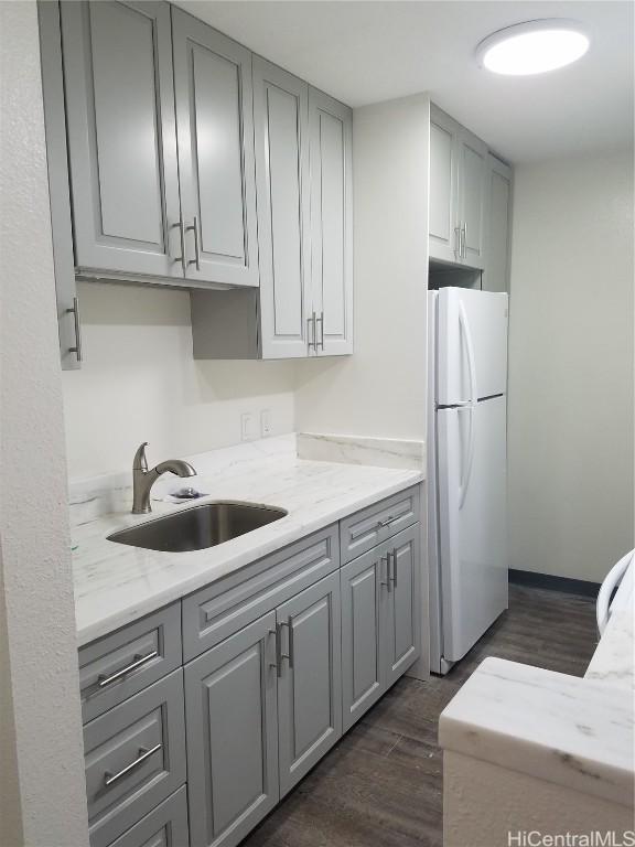 kitchen featuring light stone counters, a sink, gray cabinets, freestanding refrigerator, and dark wood finished floors