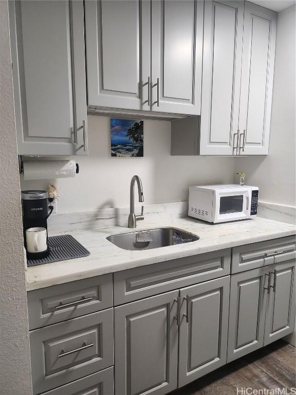 kitchen with a sink, gray cabinetry, and white microwave