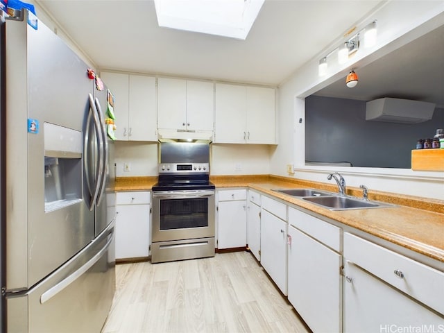 kitchen with sink, appliances with stainless steel finishes, a skylight, white cabinets, and light wood-type flooring