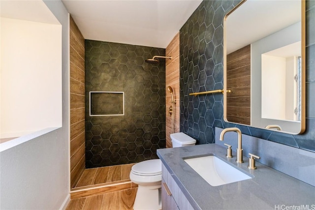 bathroom featuring toilet, wood-type flooring, tile walls, a tile shower, and vanity