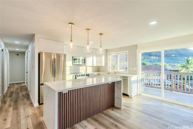 kitchen featuring sink, appliances with stainless steel finishes, a center island, white cabinets, and decorative light fixtures