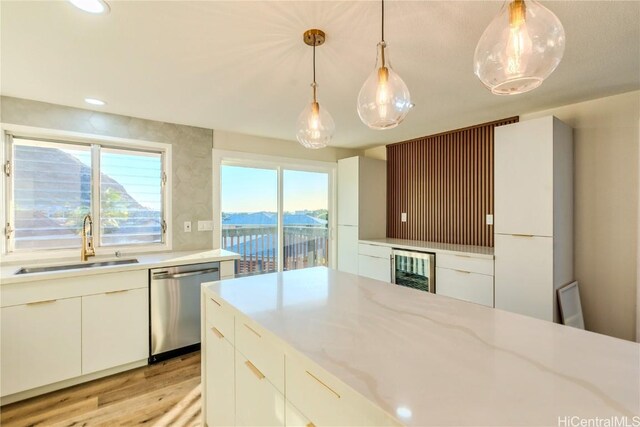 kitchen featuring sink, white cabinetry, light stone counters, decorative light fixtures, and stainless steel dishwasher