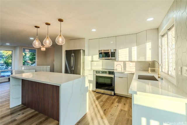 kitchen with sink, hanging light fixtures, light wood-type flooring, appliances with stainless steel finishes, and white cabinets