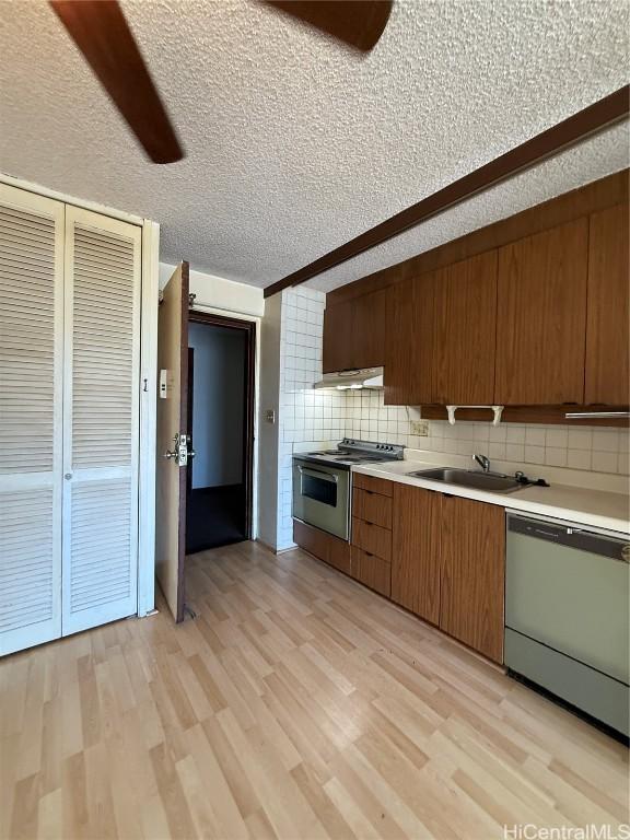 kitchen with sink, a textured ceiling, light hardwood / wood-style flooring, appliances with stainless steel finishes, and backsplash