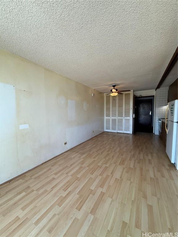 unfurnished living room with ceiling fan, a textured ceiling, and light hardwood / wood-style flooring