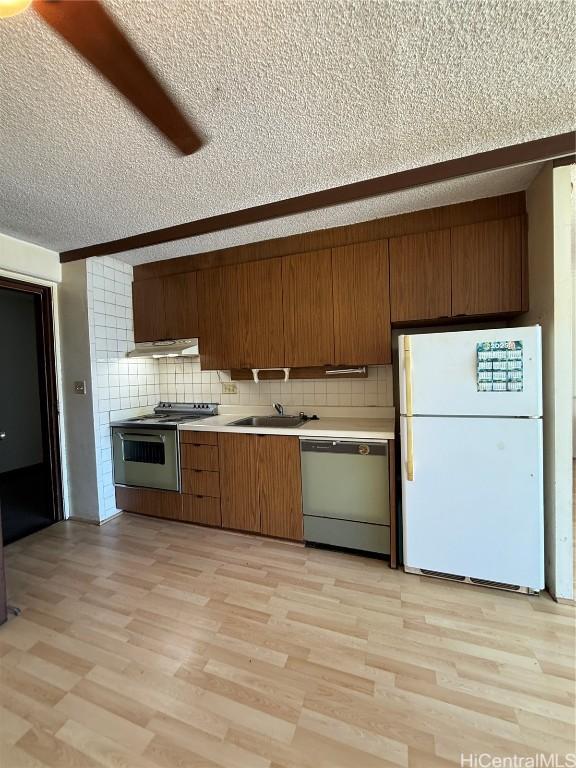 kitchen featuring sink, a textured ceiling, light hardwood / wood-style flooring, stainless steel appliances, and decorative backsplash