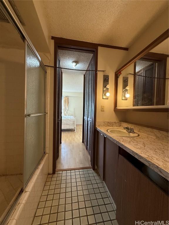 bathroom with tile patterned flooring, vanity, a textured ceiling, and bath / shower combo with glass door