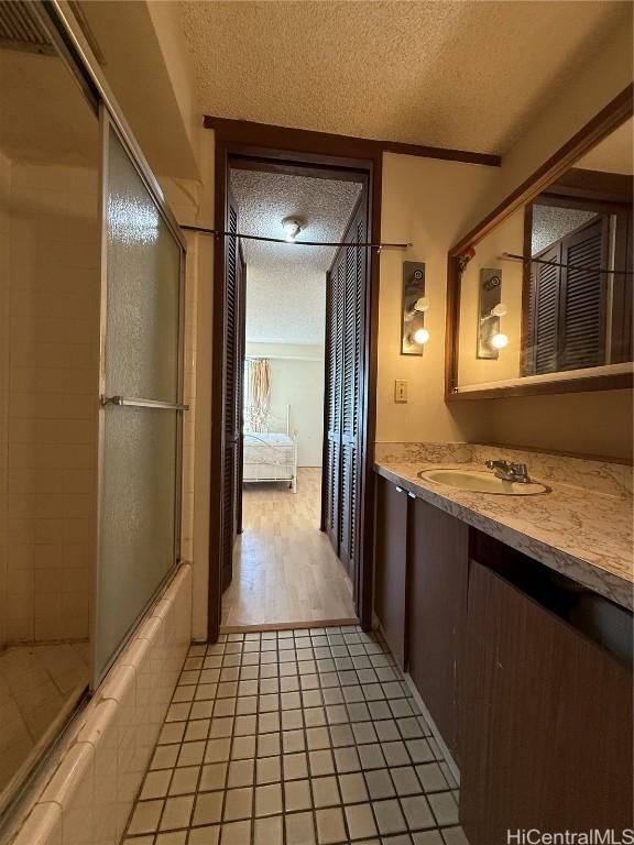 bathroom with tile patterned flooring, vanity, enclosed tub / shower combo, and a textured ceiling