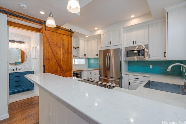 kitchen featuring pendant lighting, white cabinetry, appliances with stainless steel finishes, and a barn door