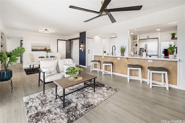 living room with ceiling fan, sink, and light wood-type flooring