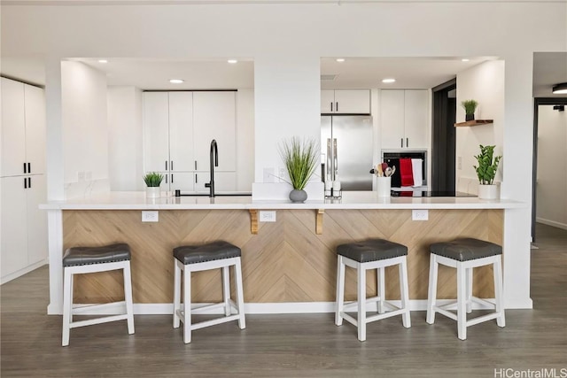 kitchen featuring a breakfast bar area, high end refrigerator, kitchen peninsula, and white cabinets