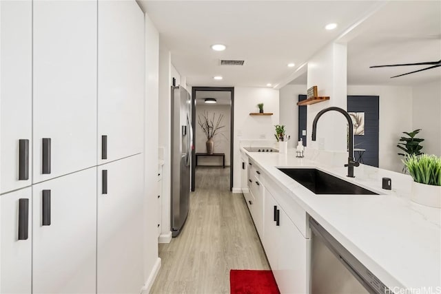 kitchen featuring appliances with stainless steel finishes, white cabinetry, sink, light stone counters, and light wood-type flooring