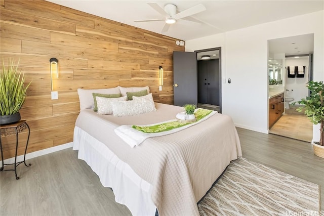 bedroom featuring ceiling fan, wood-type flooring, ensuite bathroom, and wood walls