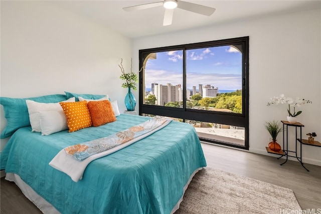 bedroom with ceiling fan, a city view, wood finished floors, baseboards, and access to outside