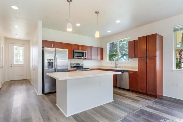 kitchen with stainless steel appliances, light countertops, a sink, a kitchen island, and light wood-type flooring