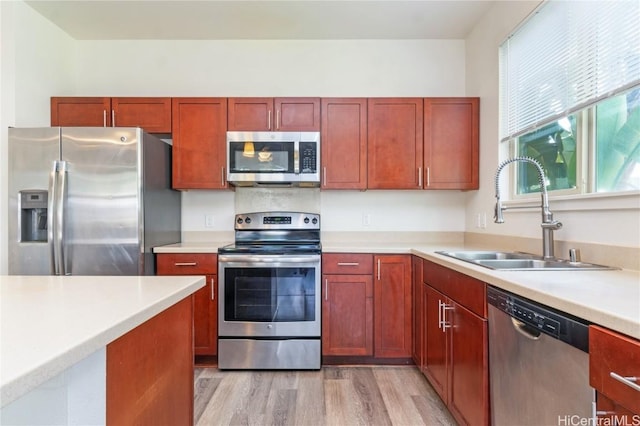 kitchen with stainless steel appliances, light countertops, a sink, dark brown cabinets, and light wood-type flooring