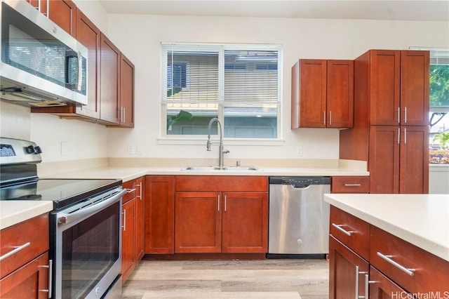 kitchen with light wood-style flooring, stainless steel appliances, a sink, and light countertops