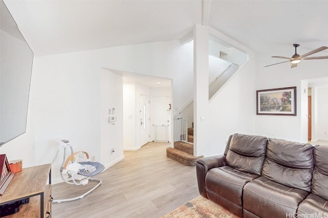 living room with baseboards, ceiling fan, stairway, vaulted ceiling, and light wood-style floors