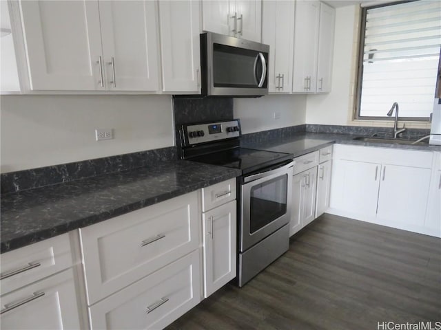 kitchen featuring dark wood-type flooring, sink, white cabinetry, dark stone countertops, and appliances with stainless steel finishes