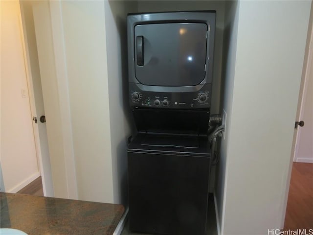 laundry area featuring stacked washer / drying machine and dark wood-type flooring