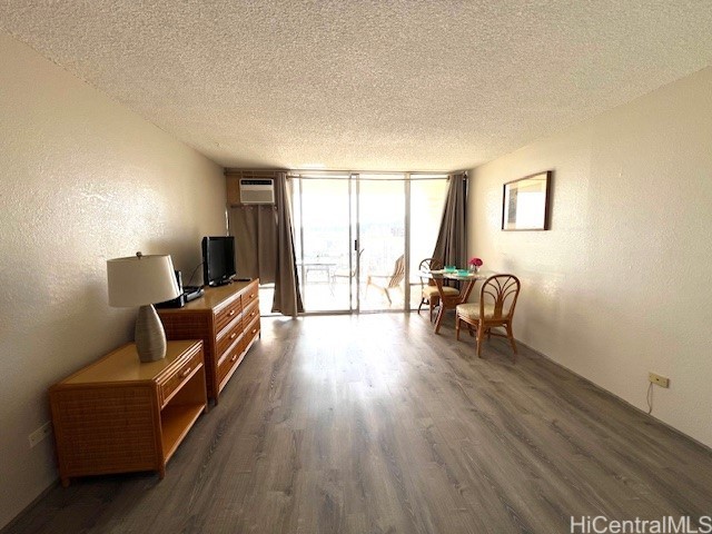 living area with a wall of windows, dark hardwood / wood-style floors, a wall unit AC, and a textured ceiling