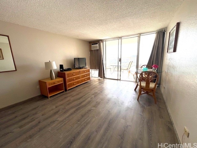 sitting room featuring dark wood-type flooring, a wall of windows, a wall mounted air conditioner, and a textured ceiling