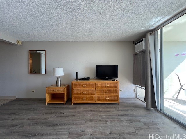 bedroom with a wall mounted air conditioner, hardwood / wood-style flooring, and a textured ceiling