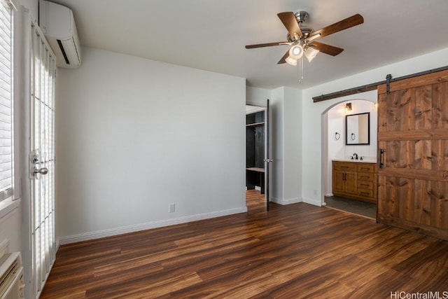 unfurnished bedroom featuring dark wood-type flooring, a wall unit AC, ceiling fan, and ensuite bathroom