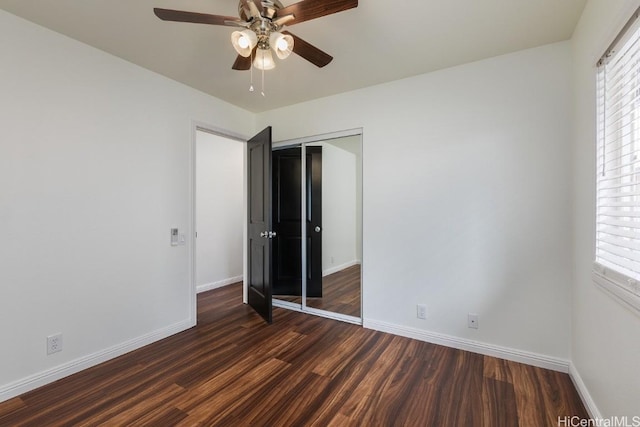 unfurnished bedroom featuring multiple windows, dark wood-type flooring, ceiling fan, and a closet