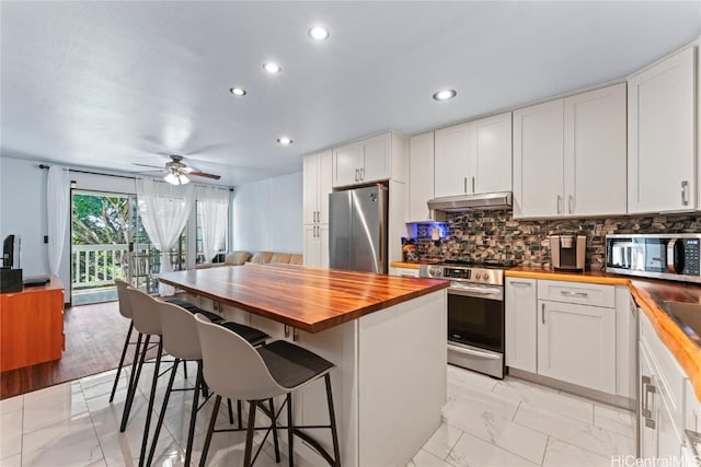 kitchen featuring white cabinetry, stainless steel appliances, a kitchen breakfast bar, and butcher block counters