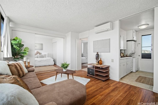 living room featuring an AC wall unit, a textured ceiling, and light hardwood / wood-style flooring