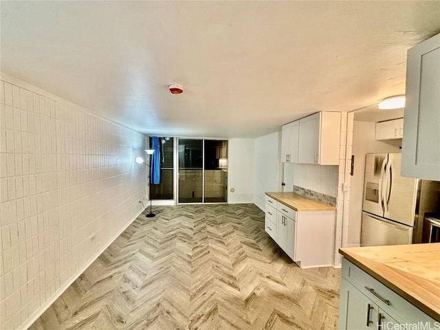 kitchen with stainless steel refrigerator with ice dispenser, light parquet flooring, butcher block countertops, and white cabinets