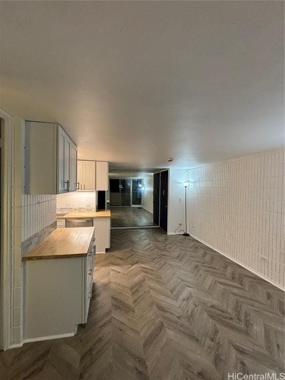 kitchen featuring butcher block counters, white cabinetry, parquet flooring, and dishwasher