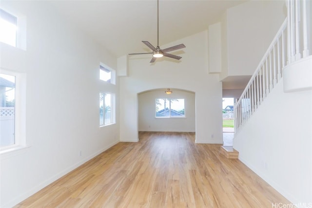 unfurnished living room with light hardwood / wood-style floors, ceiling fan, and a high ceiling