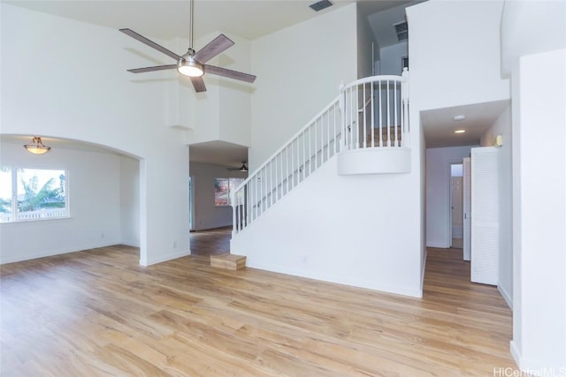 unfurnished living room with a high ceiling, ceiling fan, and light wood-type flooring