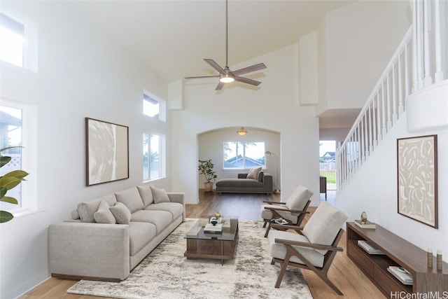 living room with a ceiling fan, wood finished floors, baseboards, a towering ceiling, and stairs